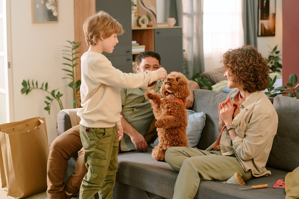 Child feeding small dog while parents watch in living room, warm family moment