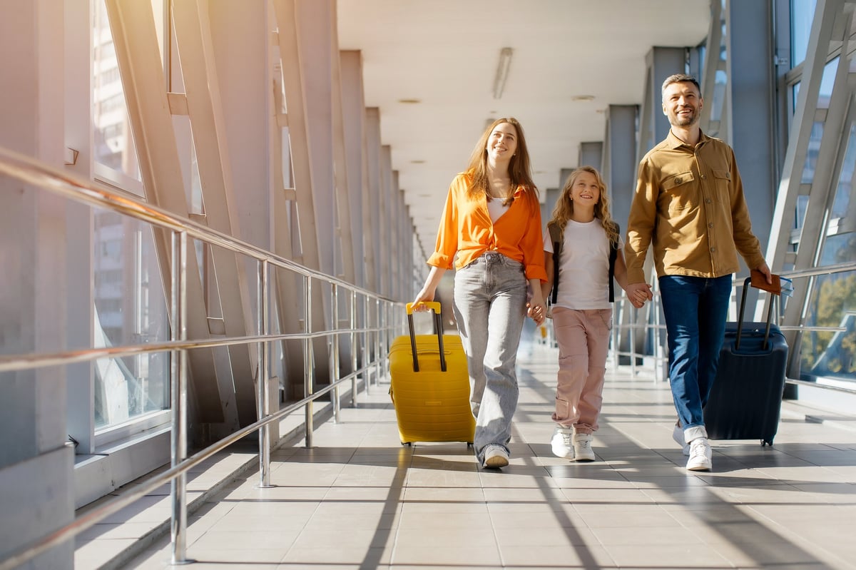 Family walking together at airport with luggage, smiling in bright corridor